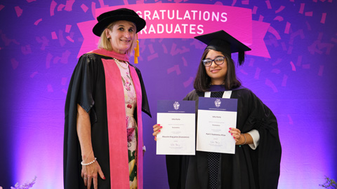 Three people at a graduation ceremony; two in academic regalia holding certificates, one in formal attire.
